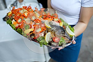 The waitress holds baked salmon with vegetables and lemon on a platter