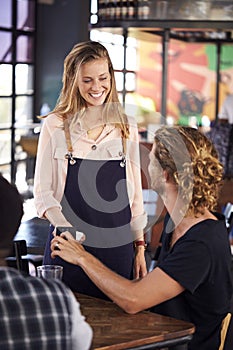 Waitress Holds Card Machine As Customer Makes Contactless Payment For Bill Using Mobile Phone