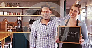Waitress and man standing with open sign on slate in cafÃ©