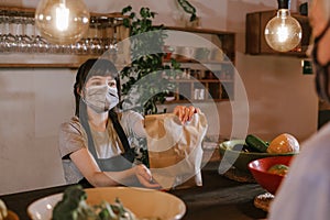 Waitress with mask giving a take away order to a customer during Coronavirus pandemic