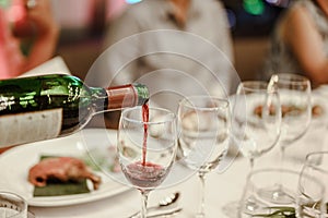 Waitress is pouring red wine in glasses for wine tasting event on the table in restaurant .