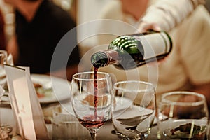 Waitress is pouring red wine in glasses for wine tasting event on the table in restaurant .