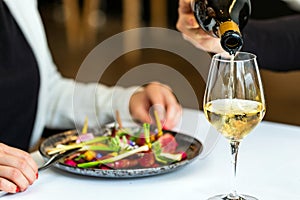 Waitress pouring white wine at table next to woman