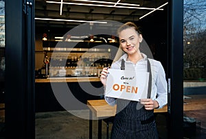 Waitress at restaurant entrance showing open sign to customers. 