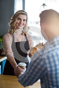 Waitress serving a cup of coffee and croissant to customer