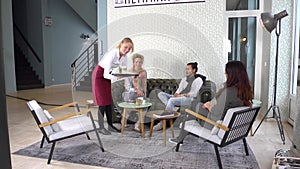 Waitress serving drinks to a group of customers of a cafe sitting in a retro styled lounge area of the bar