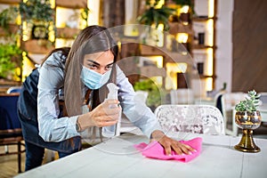 Waitress wearing protective face mask while disinfecting tables at restaurant or caffee for next customer. Corona virus and small