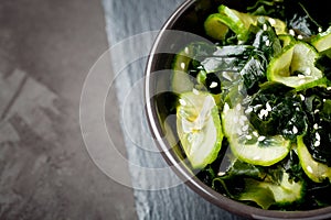 Wakame salad raw seaweed with cucumber slices and sesame in bowl on dark gray background close-up