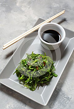 Wakame seaweed salad with sesame seeds and chili pepper in a bowl on concrete background