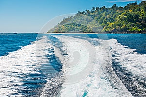 Wake of boat on water surface beside island coast