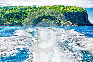 Wake of boat on water surface beside island coast