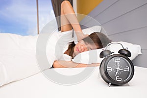 Wake up, Asian woman in bed extending hand to alarm clock. girl turns off the alarm clock waking up in the morning. Young sleeping