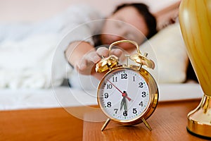 6.30 wake up call: young brunette man or woman pulling hand off the bed to the alarm clock on the foreground photo