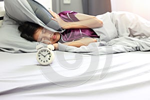 Wake up concept - In bedroom , Asian girl covering her ear with pillow from alarm clock noise in the morning. Upset asian girl