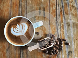 Wake up with love shape latte art coffee in the white cup and roasted coffee beans in spoon on the vintage wooden