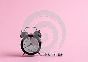 Wake up message and black clock on a pastel pink background