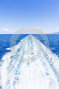 Wake of water from a boat, open sea with horizon and blue sky