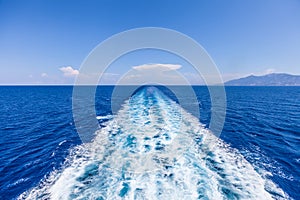 Wake of water from a boat, open sea with horizon and blue sky