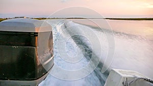 Wake and waves and close up of an outboard engine in coastal waters at sunset with marsh grass in the background