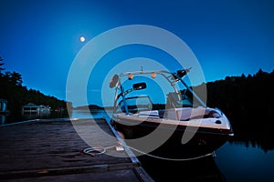 A wakeboard boat docked on Lake Joseph in the evening with the moon in the background.