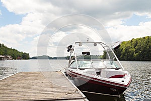 A wakeboard boat at a wooden dock in the Muskokas on a sunny day.