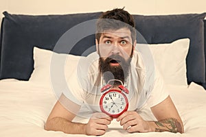 Waking up early gives more time to prepare and be timely. Hipster bearded man lay in bed with alarm clock. Time to wake