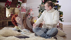 Waking up woman scaring man kissing wife on cheek. Joyful Caucasian husband and spouse having fun on Christmas eve at