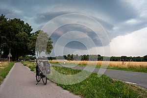Walbeck, North Rine-Westphalia, Germany - Trekking bike at a country road with a hugh cumulus rain cloud in the background
