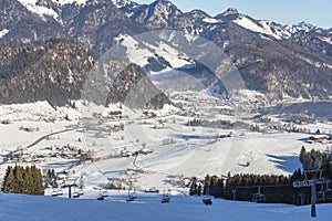 Walchsee village in a mountain valley on a sunny winter day with a ski lift