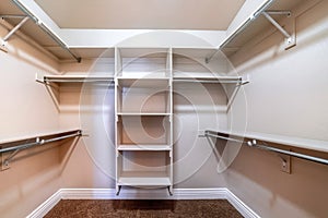 Walk in closet with empty storage shelves for clothes built against white wall