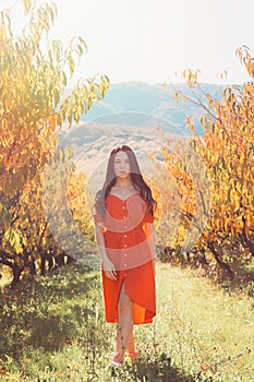 Walk in the garden. A brunette woman in a red dress walks on the grass along the trees. Vertical orientation