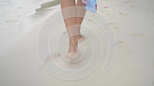 Walk on summer beach, beautiful bare female legs go along wet sand on sea coast