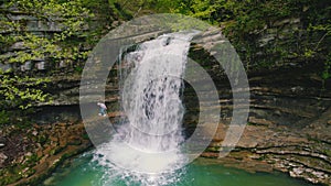 walk to Okatse Canyon - one person walking on the large stones covered with green moss under the small waterfall