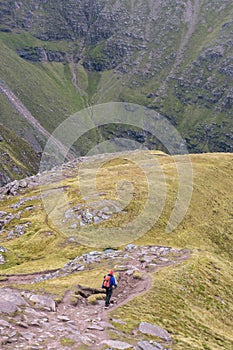 Walker with red backpack descending ridge trail in Scottish Hig