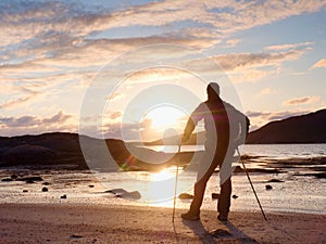 Walker watch sunny spring daybreak over sea. Hiker with backpack stand on sandy shore. Sun rays