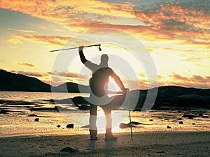 Walker watch sunny spring daybreak over sea. Hiker with backpack stand on sandy shore. Sun rays