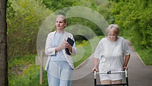 Walking with the aid of a walker, an elderly woman is accompanied by a healthcare worker nearby.