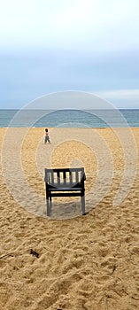 Walking alone on the beach. One wooden empty chair on beach