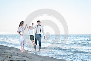 Walking along the sea shore. Wide view of mom, dad and son walking in sea