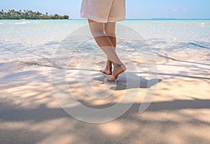 Walking on the beach. Barefoot woman in white pants walk on bright clean sandy seashore in the warm sunlight.