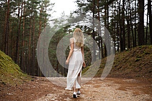 Walking Beautiful young blonde woman forest nymph in white dress in evergreen wood