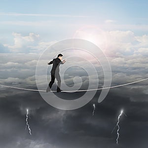 Walking businessman balancing on rope with sun sky cloudy lightning