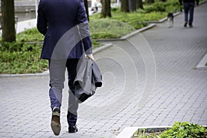 Walking businessman on sidewalk in a park. Businessman in blue business suit holding a jacket
