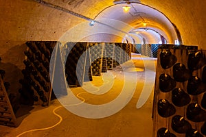 Walking in deep and long undergrounds caves with dusty bottles on racks, making champagne sparkling wine from chardonnay and pinor