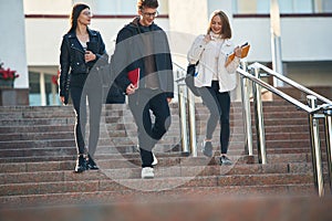 Walking down the stairs. Three young students are outside the university outdoors