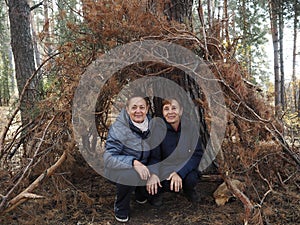 Walking elderly people in the autumn forest. Imitation of a hut made of branches. They look at the camera with optimism