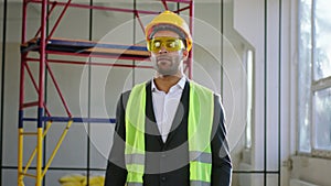 Walking in front of the camera businessman in the suit he wearing protective helmet and glasses then posing in front of