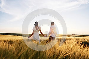 Walking and holding each other by the hands. Couple just married. Together on the majestic agricultural field at sunny day