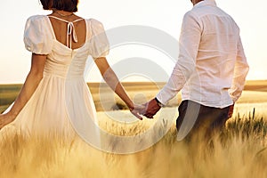 Walking and holding each other by the hands. Couple just married. Together on the majestic agricultural field at sunny day