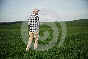 Walking, holding notepad. Handsome young man is on agricultural field
